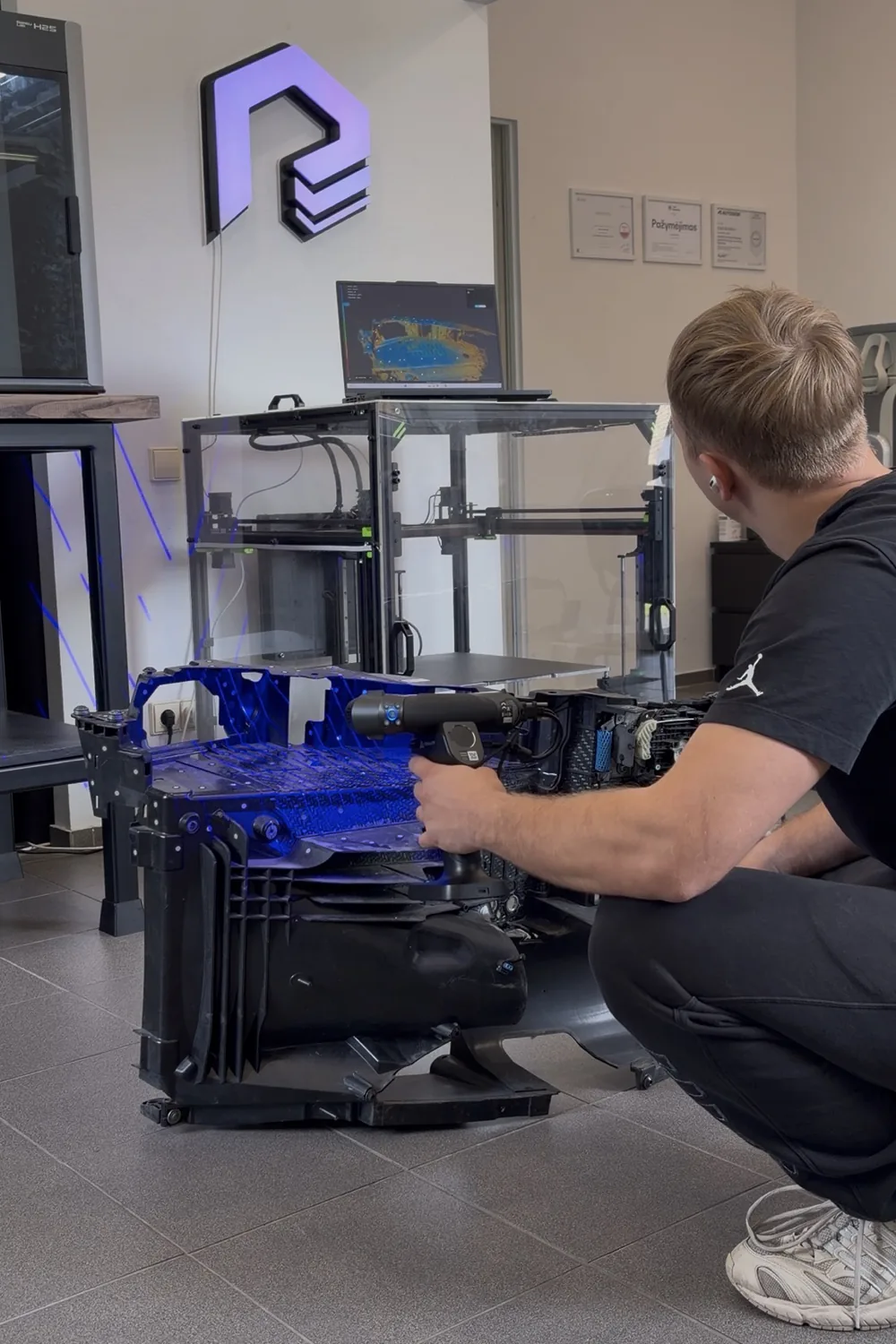 Rankiniu 3D skeneriu skenuojamas automobilio priekio karkasas, ekrane matosi skenavimo duomenys