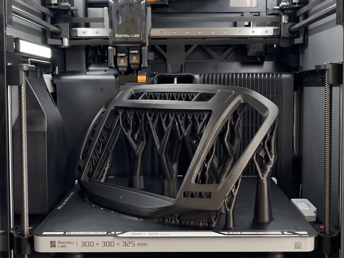 3D spausdinta juoda detalė su medžio formos atramomis ant spausdintuvo pagrindo